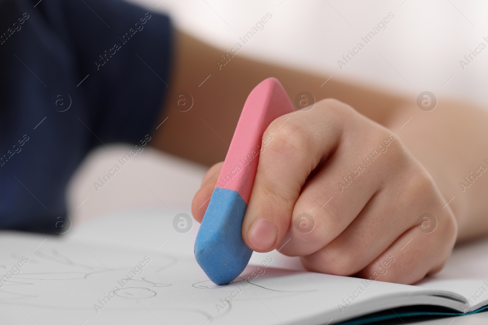 Photo of Boy erasing mistake in his notebook at white desk, closeup