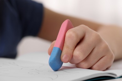 Boy erasing mistake in his notebook at white desk, closeup