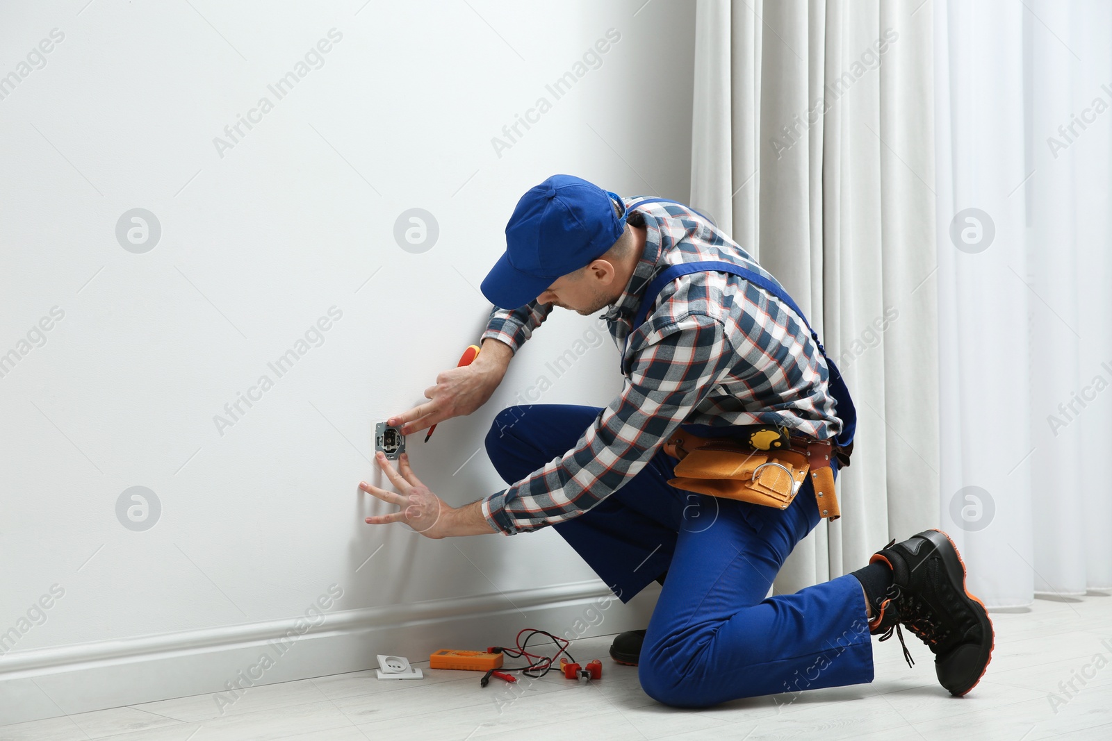 Photo of Electrician with screwdriver repairing power socket indoors