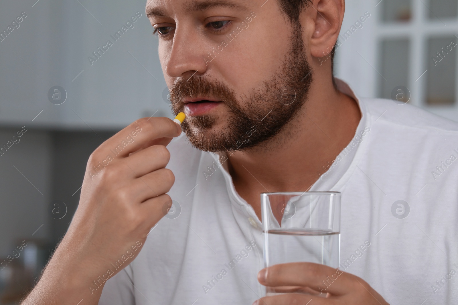 Photo of Depressed man with glass of water taking antidepressant pill indoors, closeup