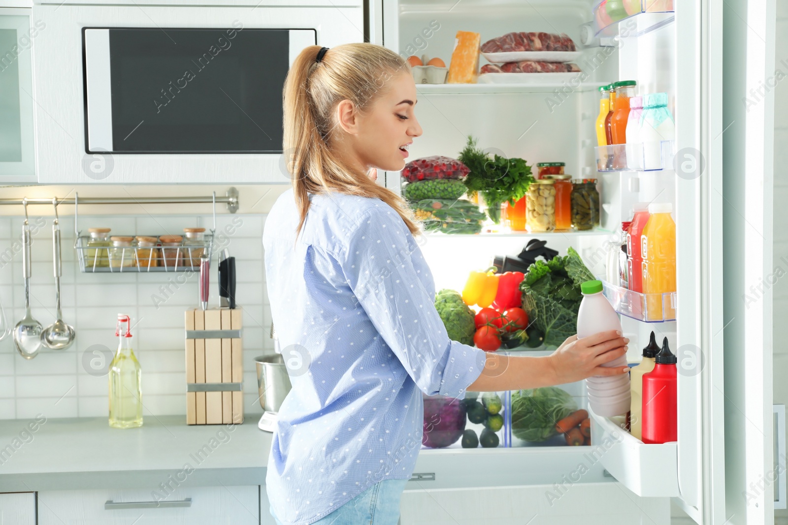 Photo of Woman taking bottle with milk out of refrigerator in kitchen