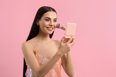 Photo of Beautiful woman with cosmetic pocket mirror applying makeup on pink background, space for text