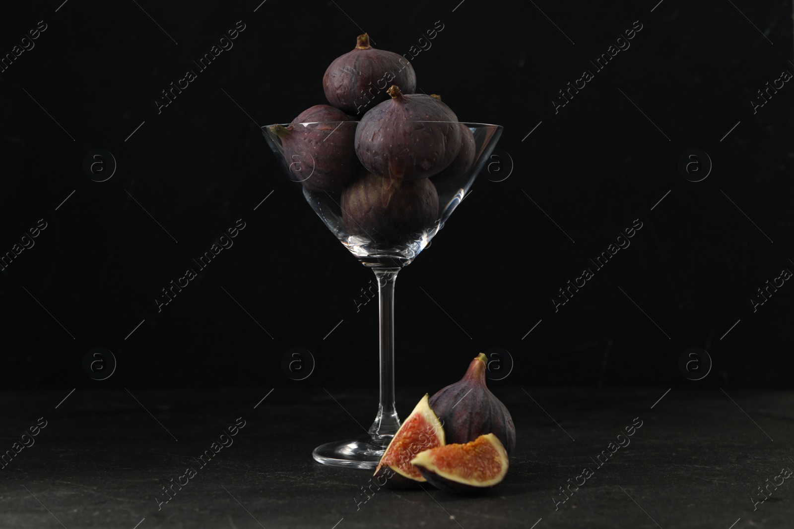 Photo of Tasty raw figs in martini glass on black table