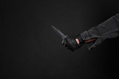 Man holding knife on black background, closeup with space for text. Dangerous criminal