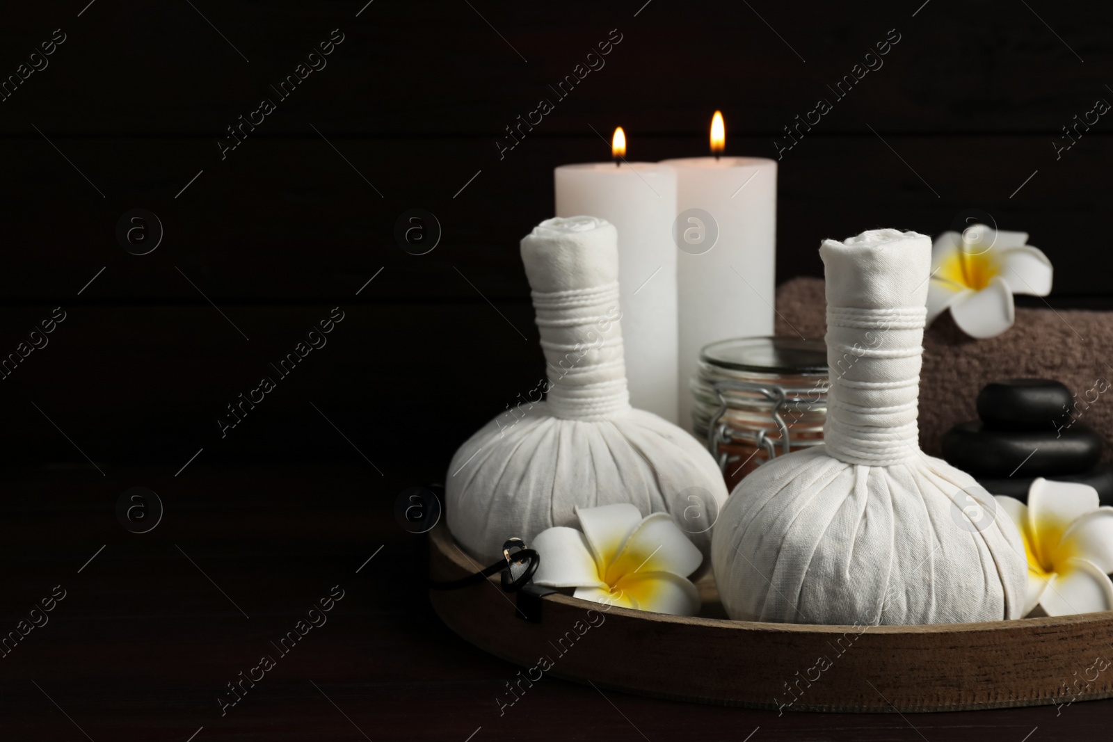 Photo of Herbal massage bags, spa stones, candles, sea salt and plumeria flowers on wooden table. Space for text