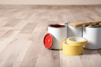 Cans of paint and decorator tools on wooden floor indoors. Space for text