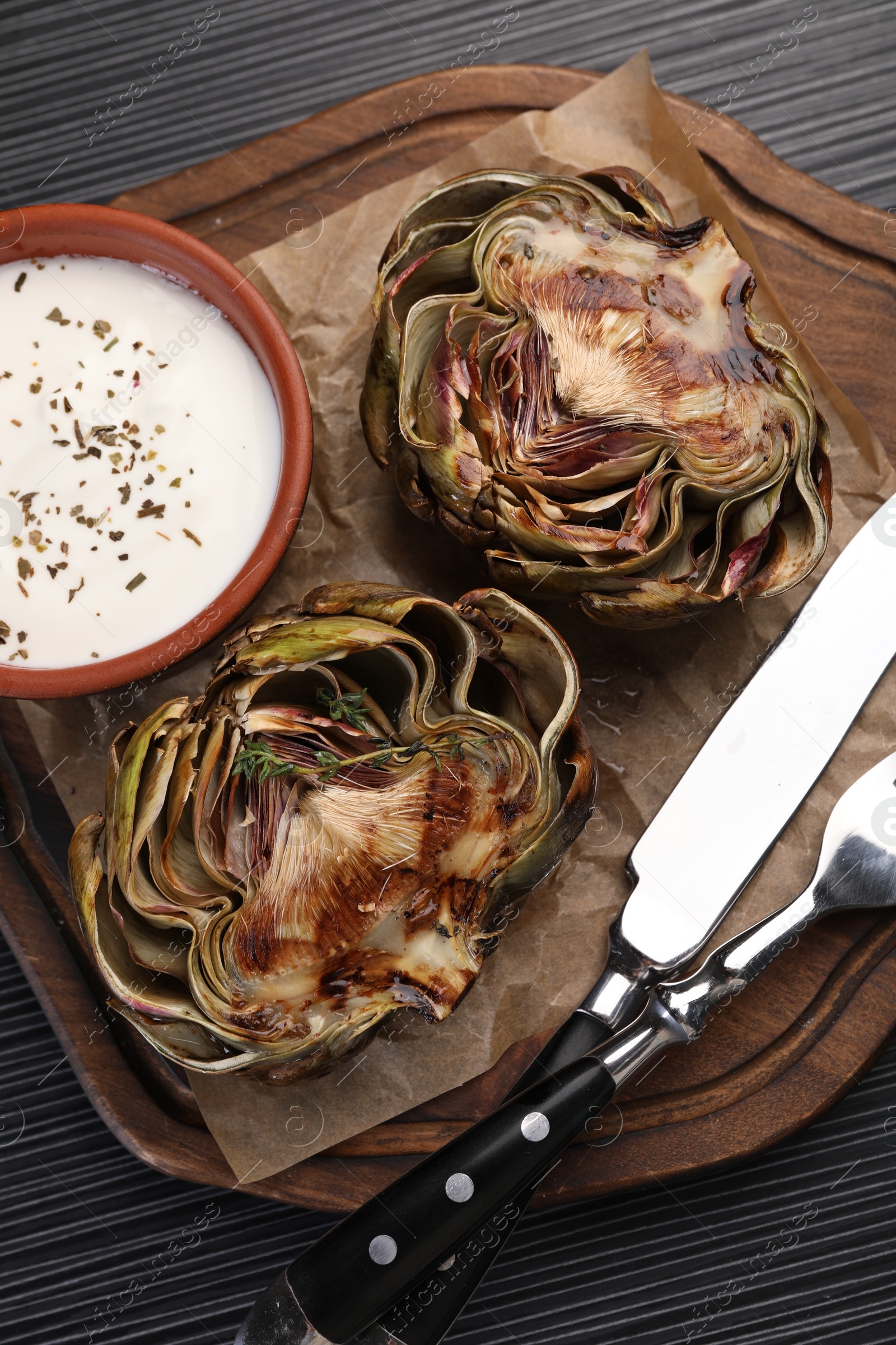 Photo of Tasty grilled artichoke and sauce on dark wooden table, top view