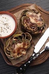 Tasty grilled artichoke and sauce on dark wooden table, top view