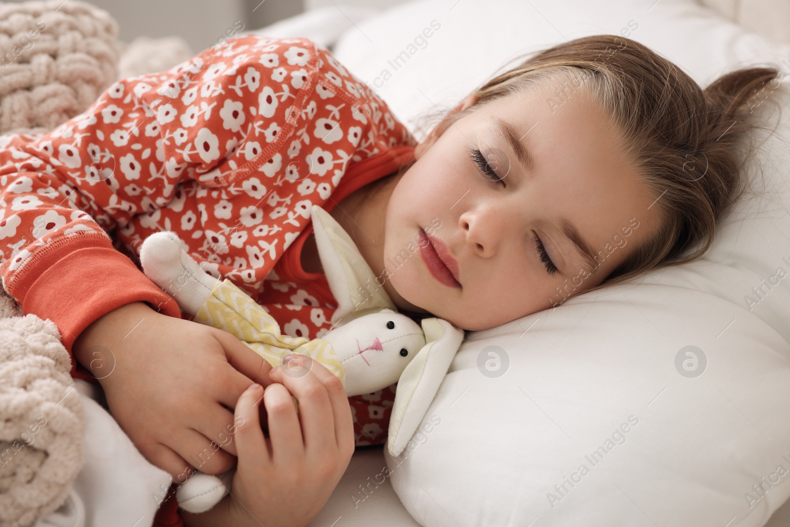 Photo of Cute little girl with toy bunny sleeping in bed at home, closeup