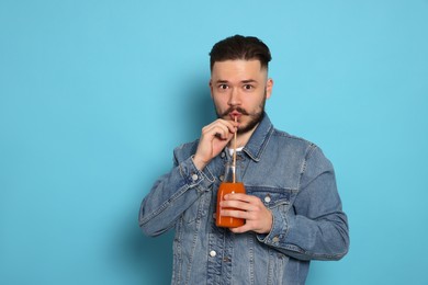 Photo of Handsome young man drinking juice from glass bottle on light blue background