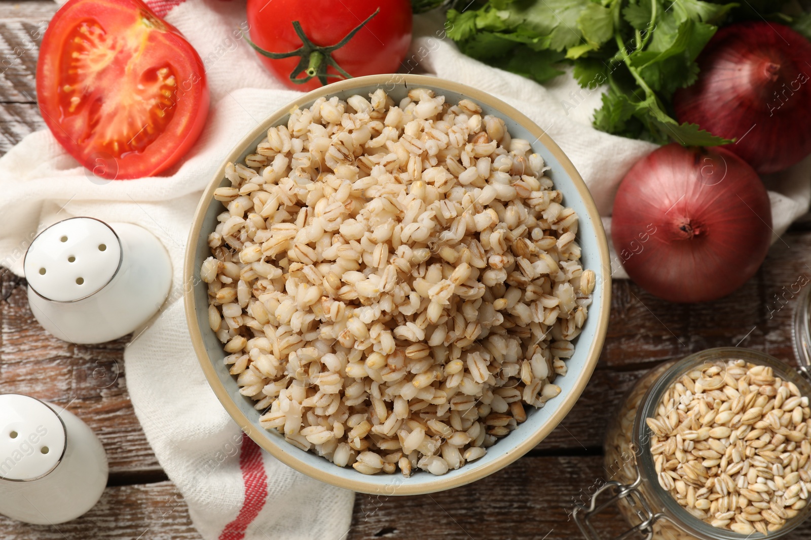 Photo of Delicious pearl barley in bowl served on wooden table, flat lay