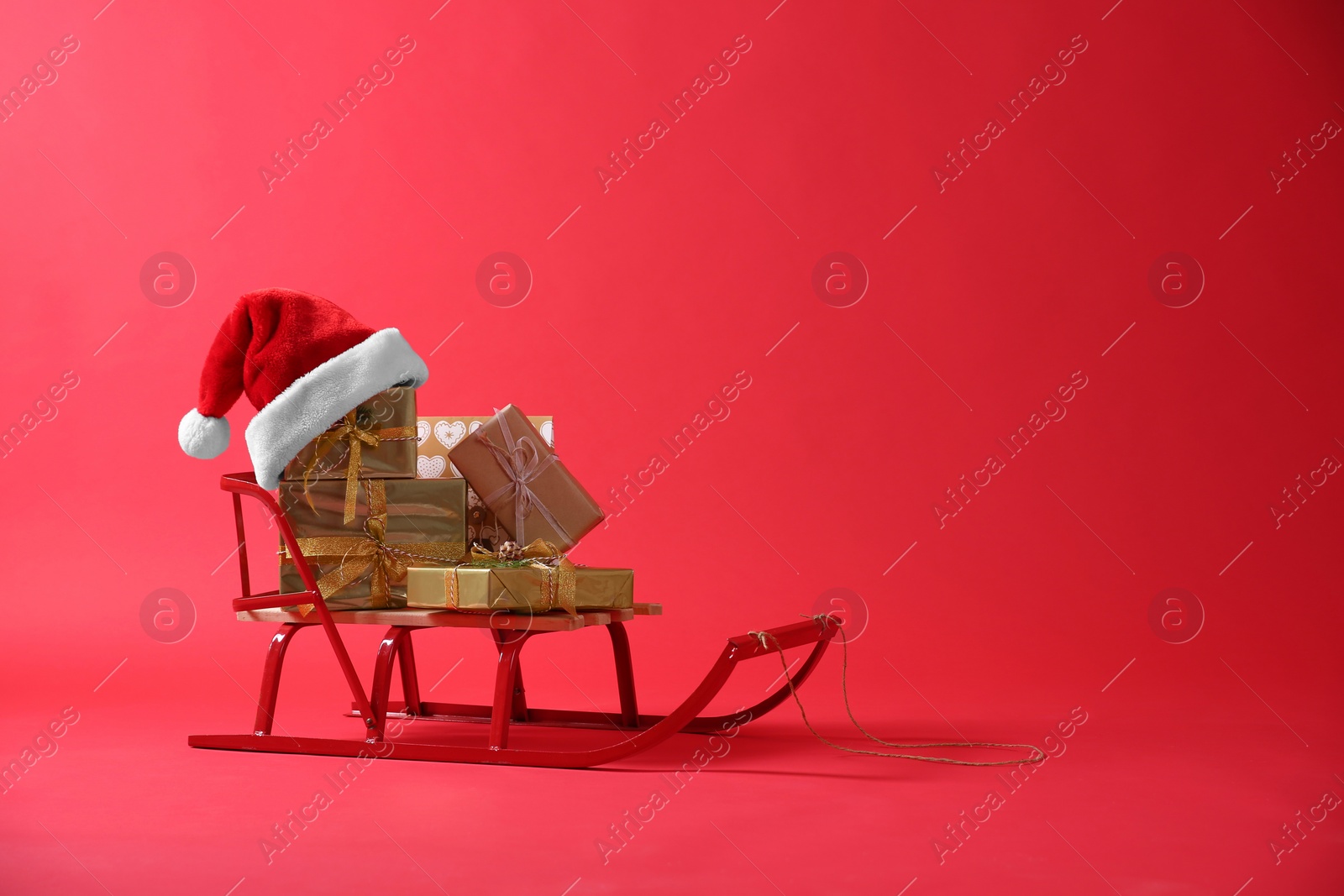 Photo of Sleigh with gift boxes and Santa hat on red background. Space for text