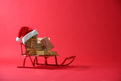 Photo of Sleigh with gift boxes and Santa hat on red background. Space for text