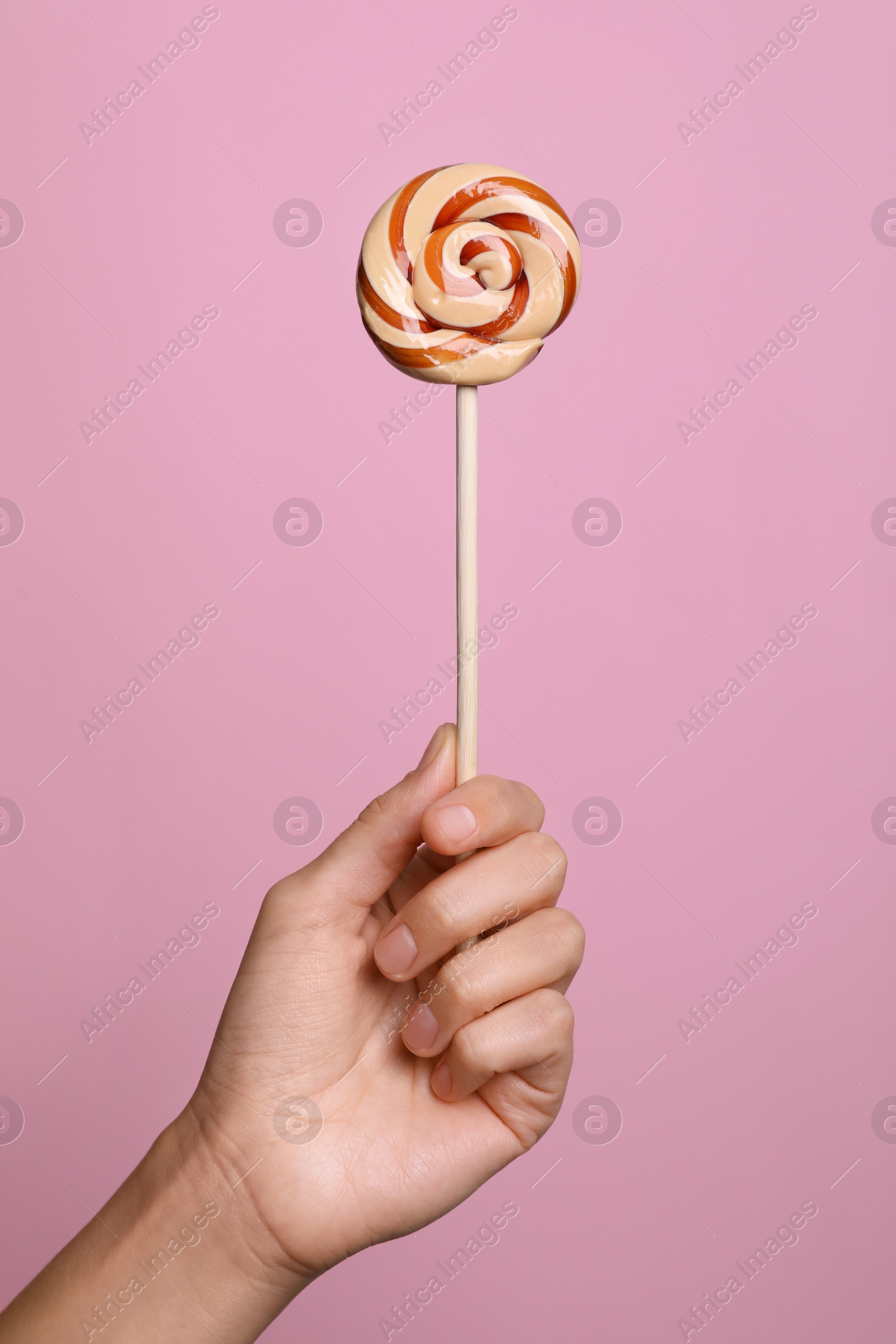 Photo of Woman holding bright tasty lollipop on pink background, closeup