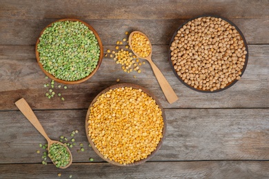 Photo of Bowls and spoons with dried peas on wooden background, flat lay