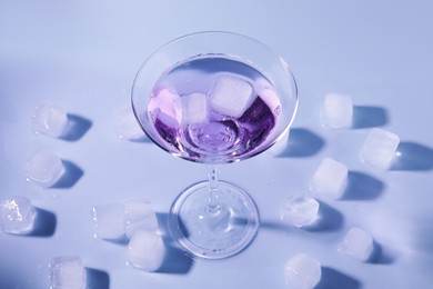 Photo of Fresh cocktail in martini glass with ice cubes on light blue background