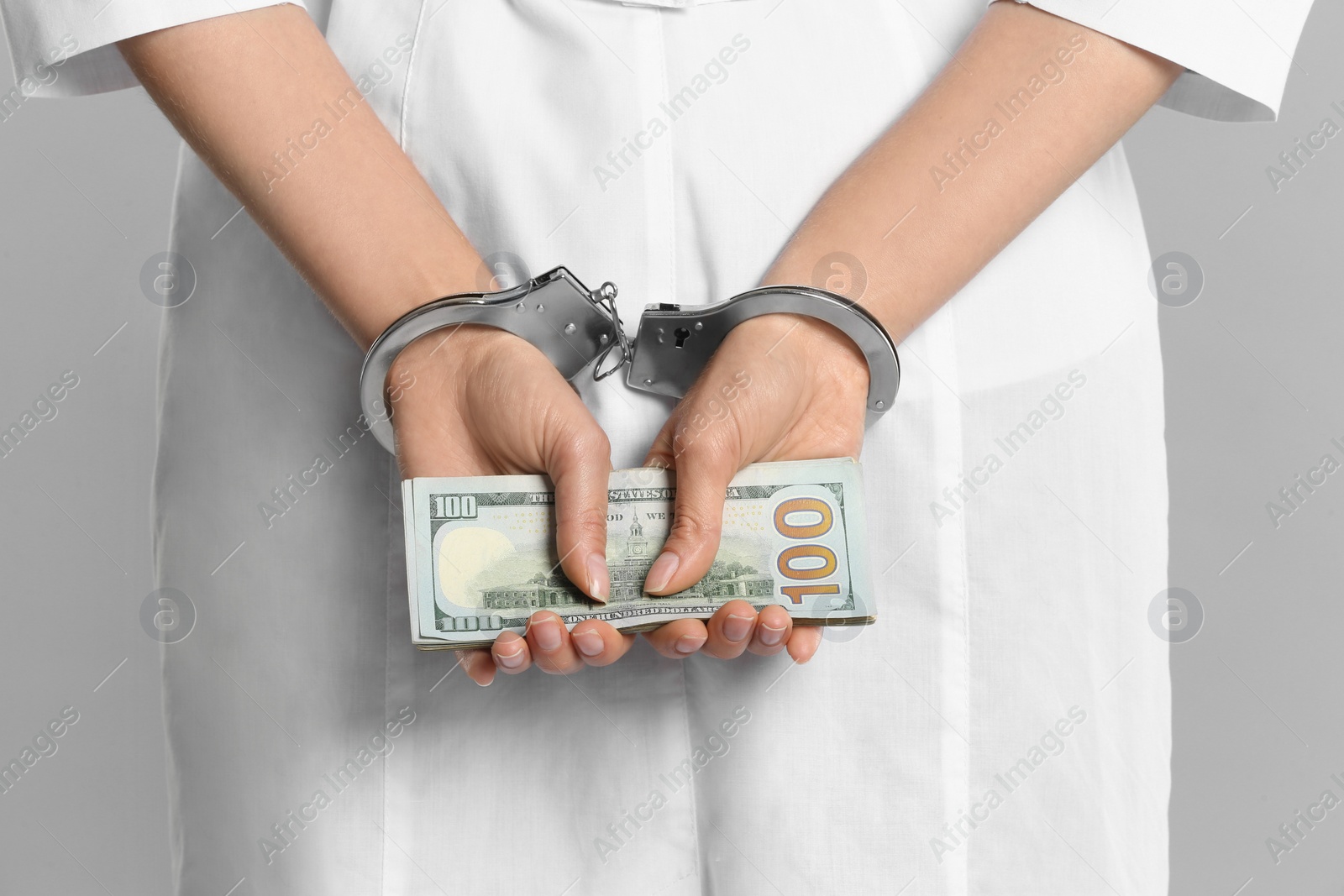 Photo of Doctor in handcuffs with bribe on grey background, closeup. Corrupted medicine