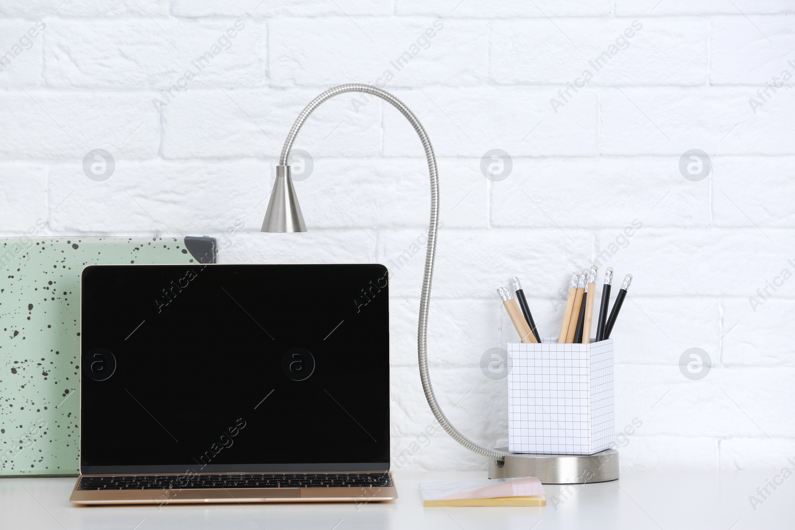 Photo of Modern workplace with laptop on table against brick wall. Mockup for design