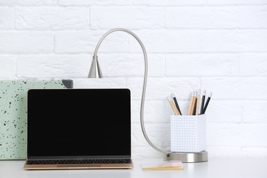 Modern workplace with laptop on table against brick wall. Mockup for design