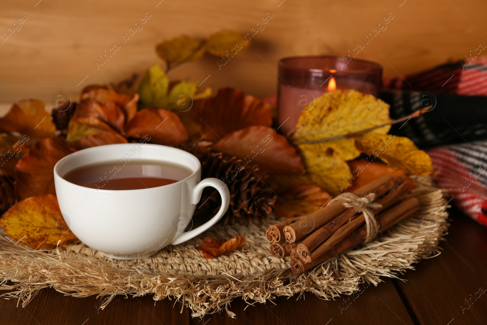Photo of Cup of hot tea, pine cone, cinnamon sticks and autumn leaves on wooden table. Space for text