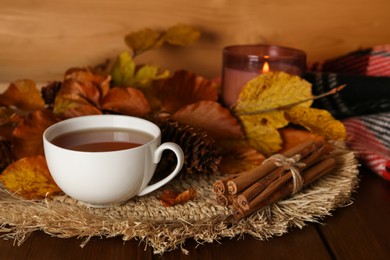 Photo of Cup of hot tea, pine cone, cinnamon sticks and autumn leaves on wooden table. Space for text