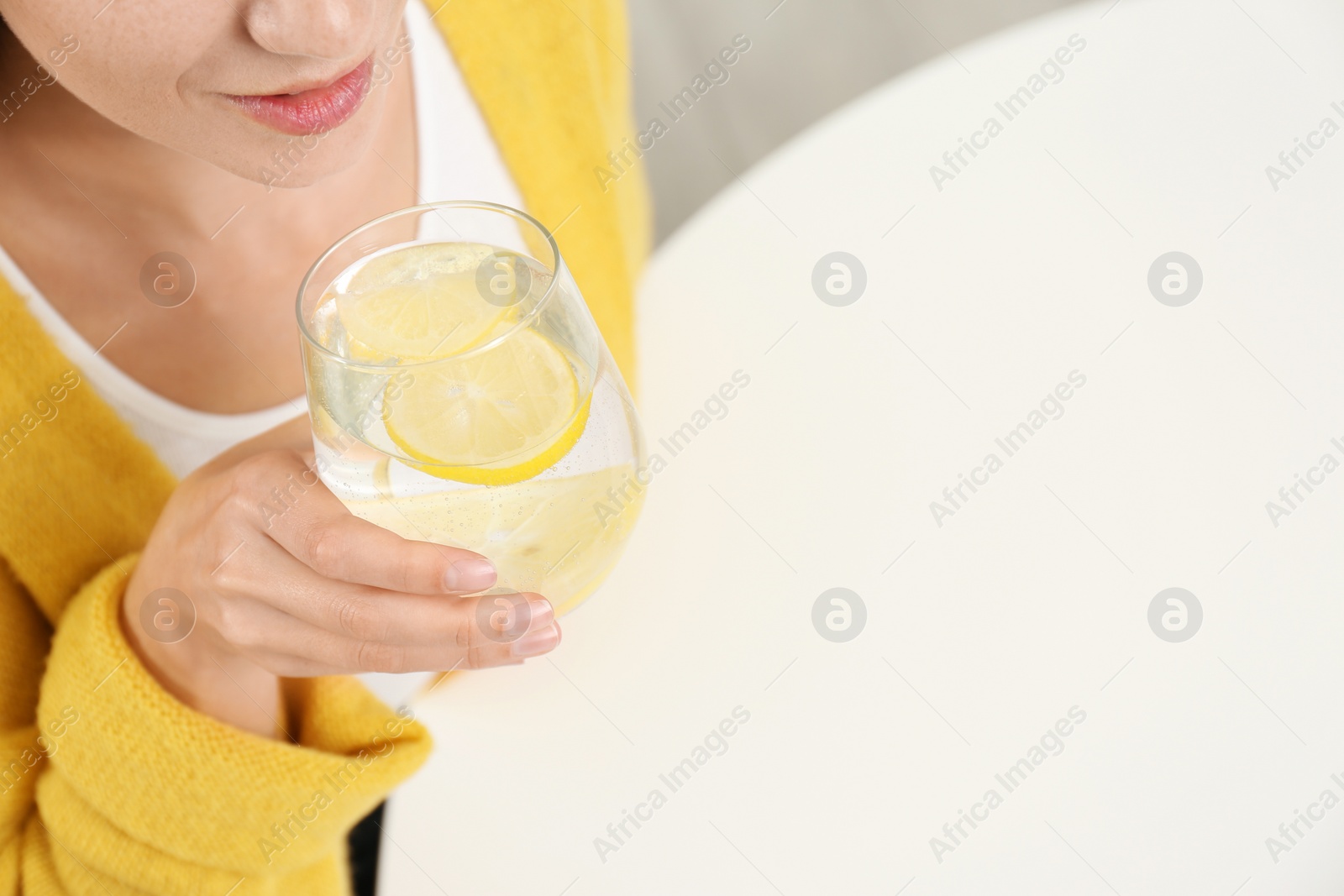 Photo of Young woman drinking lemon water at white table, above view. Space for text