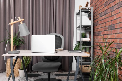 Stylish workplace with desk, chair, bookcase and potted plants at home