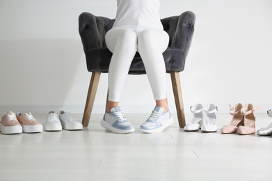 Photo of Young woman choosing shoes while sitting in armchair, closeup