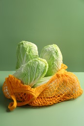 Photo of Fresh Chinese cabbages in string bag on green background