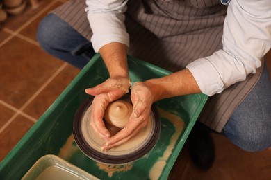 Man crafting with clay on potter's wheel indoors, closeup