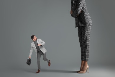 Image of Small man running from giant woman on grey background