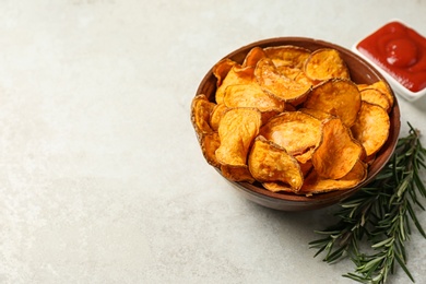 Delicious sweet potato chips in bowl, rosemary and sauce on light background. Space for text