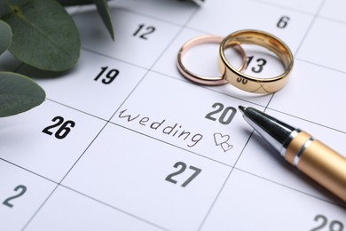 Photo of Calendar with date reminder about Wedding Day, pen and rings, closeup