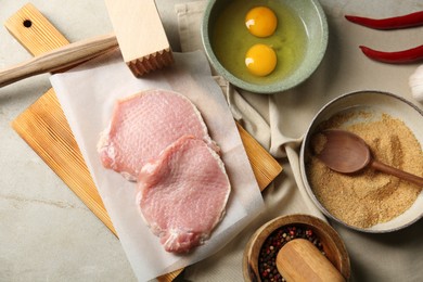 Photo of Raw pork chops, meat mallet and ingredients for cooking schnitzel on grey table, flat lay