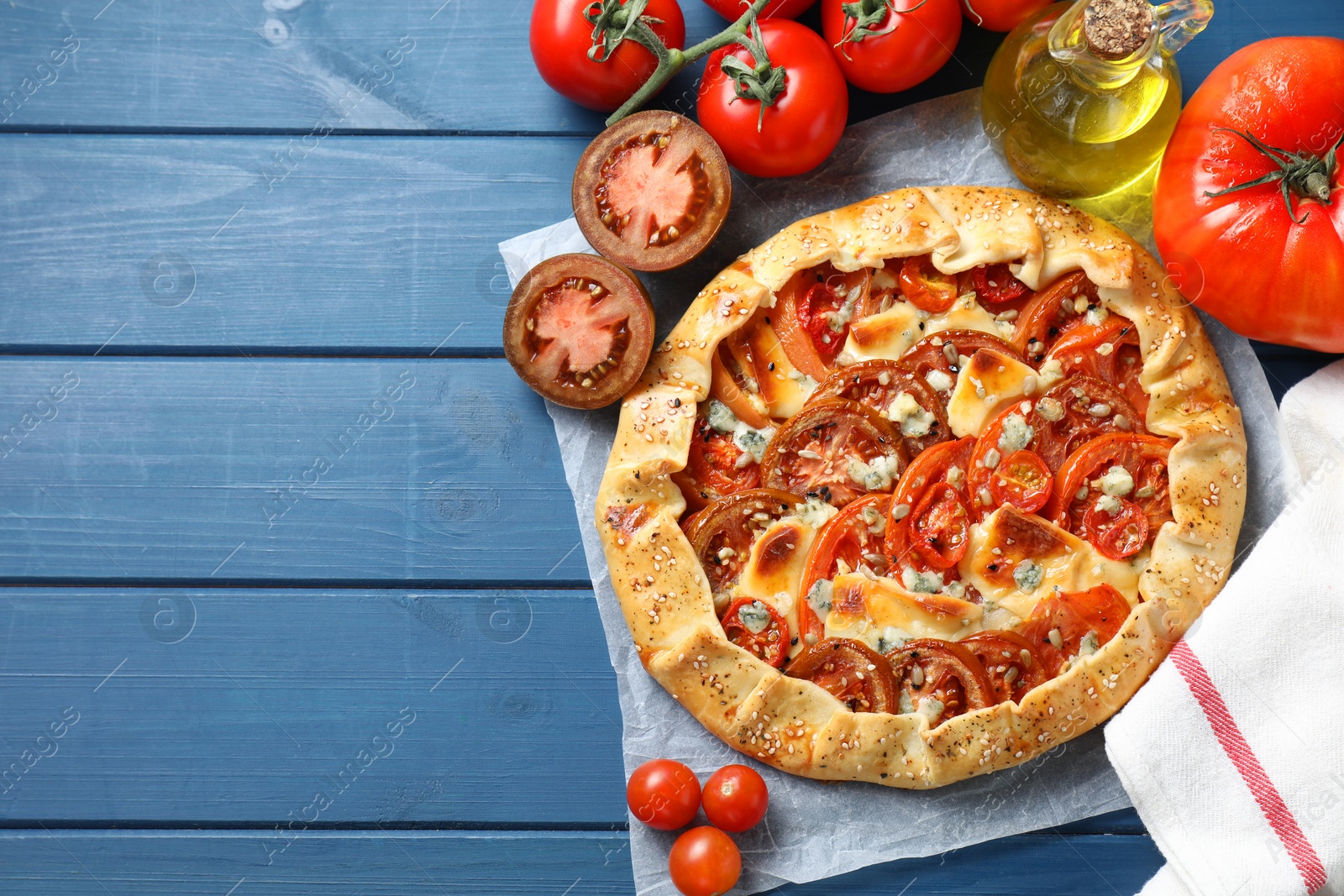 Photo of Flat lay composition of tasty galette with tomato and cheese (Caprese galette) on blue wooden table. Space for text