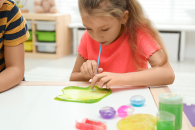 Photo of Little girl blowing slime bubble on white table indoors, closeup
