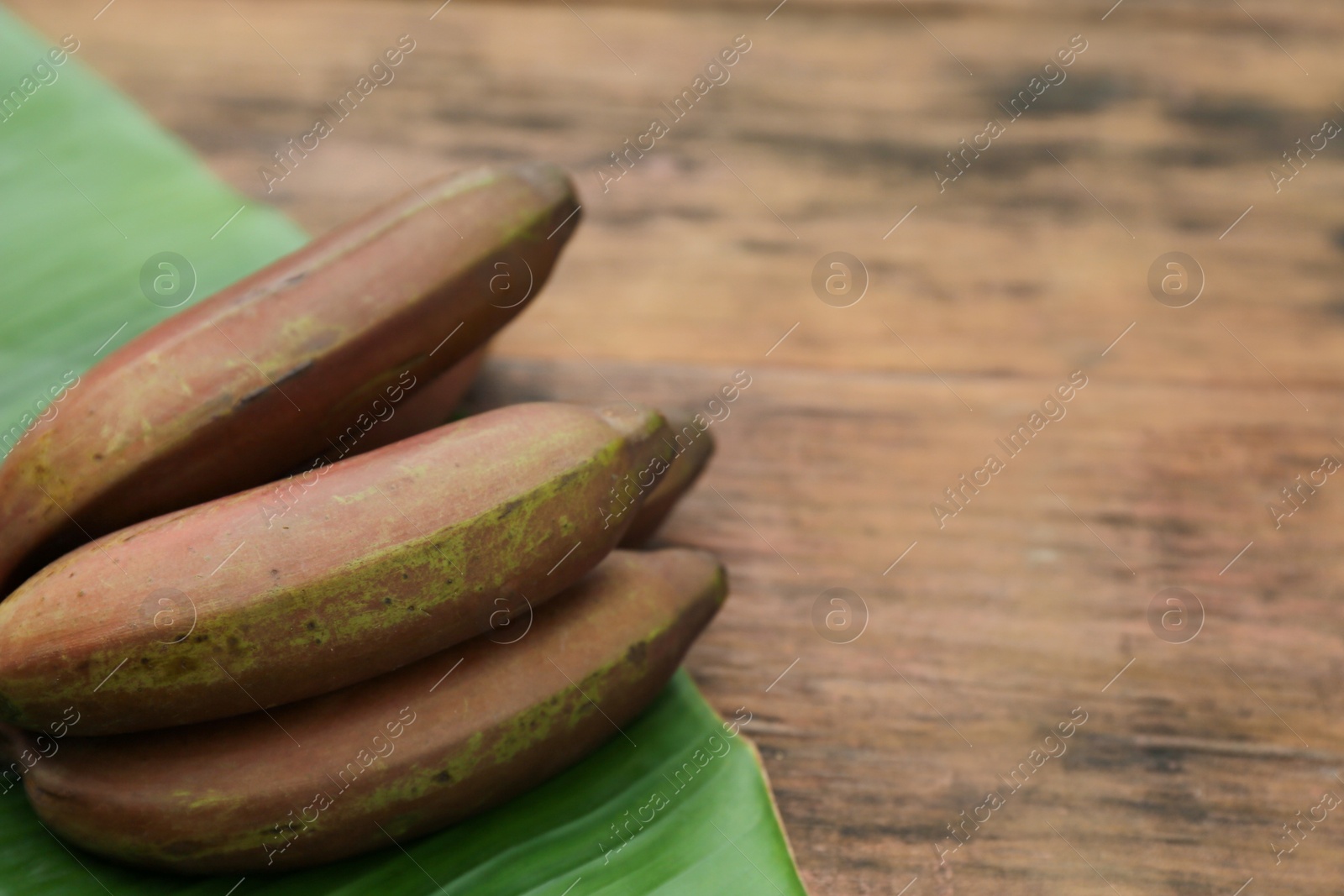 Photo of Delicious purple bananas and fresh leaf on wooden table, closeup. Space for text