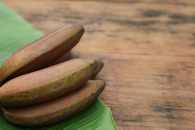 Delicious purple bananas and fresh leaf on wooden table, closeup. Space for text