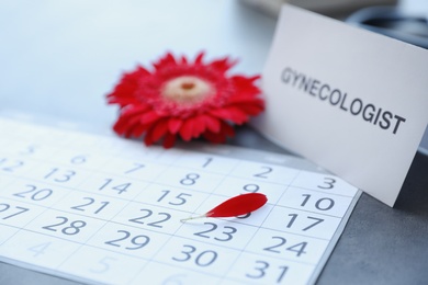 Card with word GYNECOLOGIST, calendar and red flower petal on table