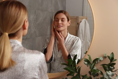 Woman massaging her face near mirror in bathroom