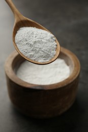 Spoon of baking powder over bowl at grey textured table, closeup