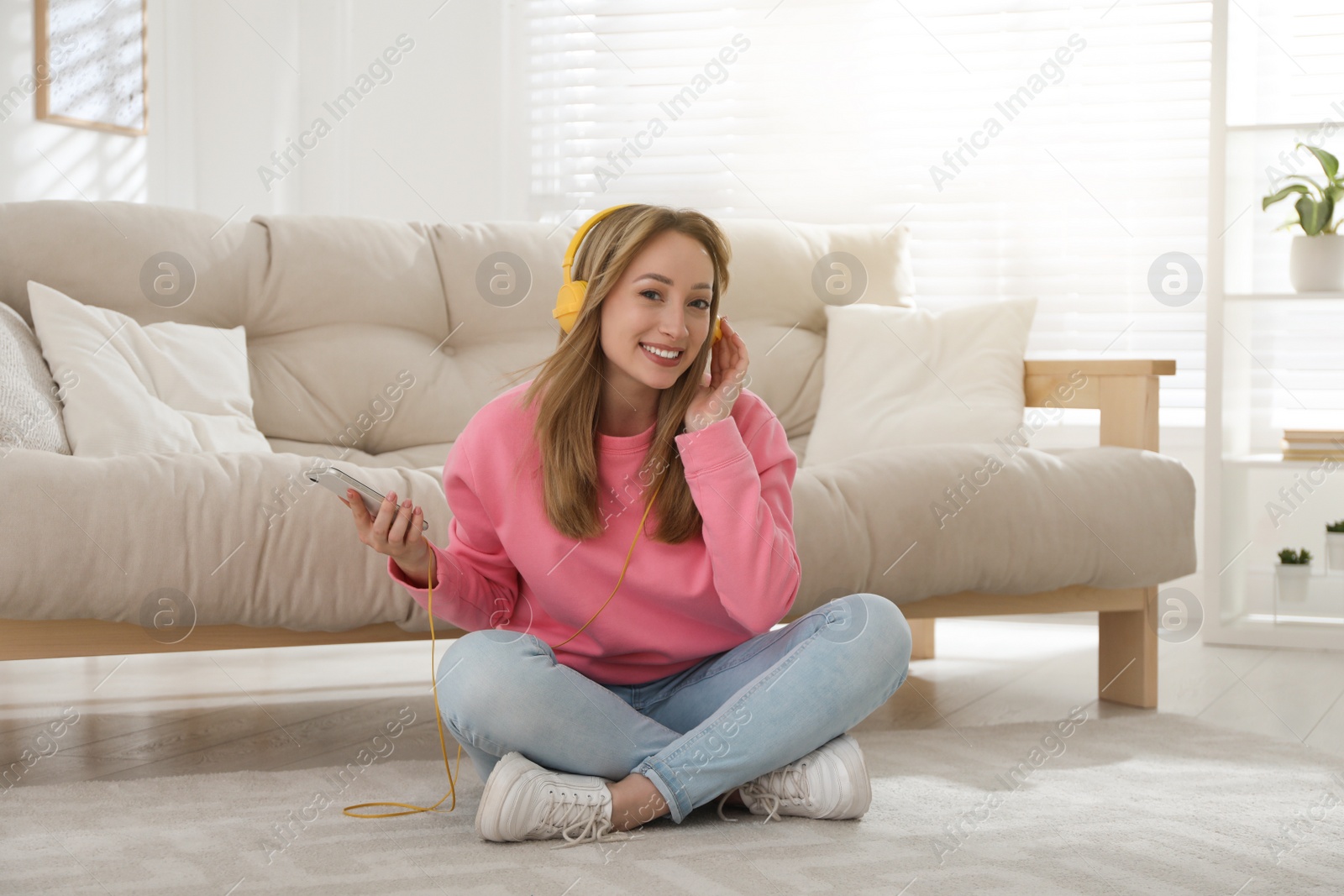 Photo of Young woman with headphones listening to music while sitting on floor in living room