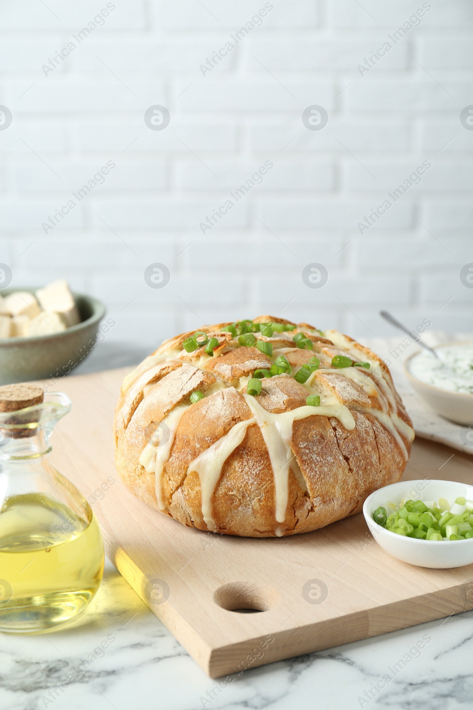 Photo of Freshly baked bread with tofu cheese, green onion and oil on white marble table