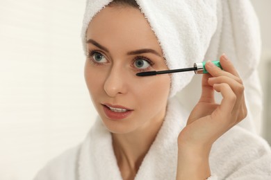 Photo of Beautiful woman applying mascara with brush indoors, closeup