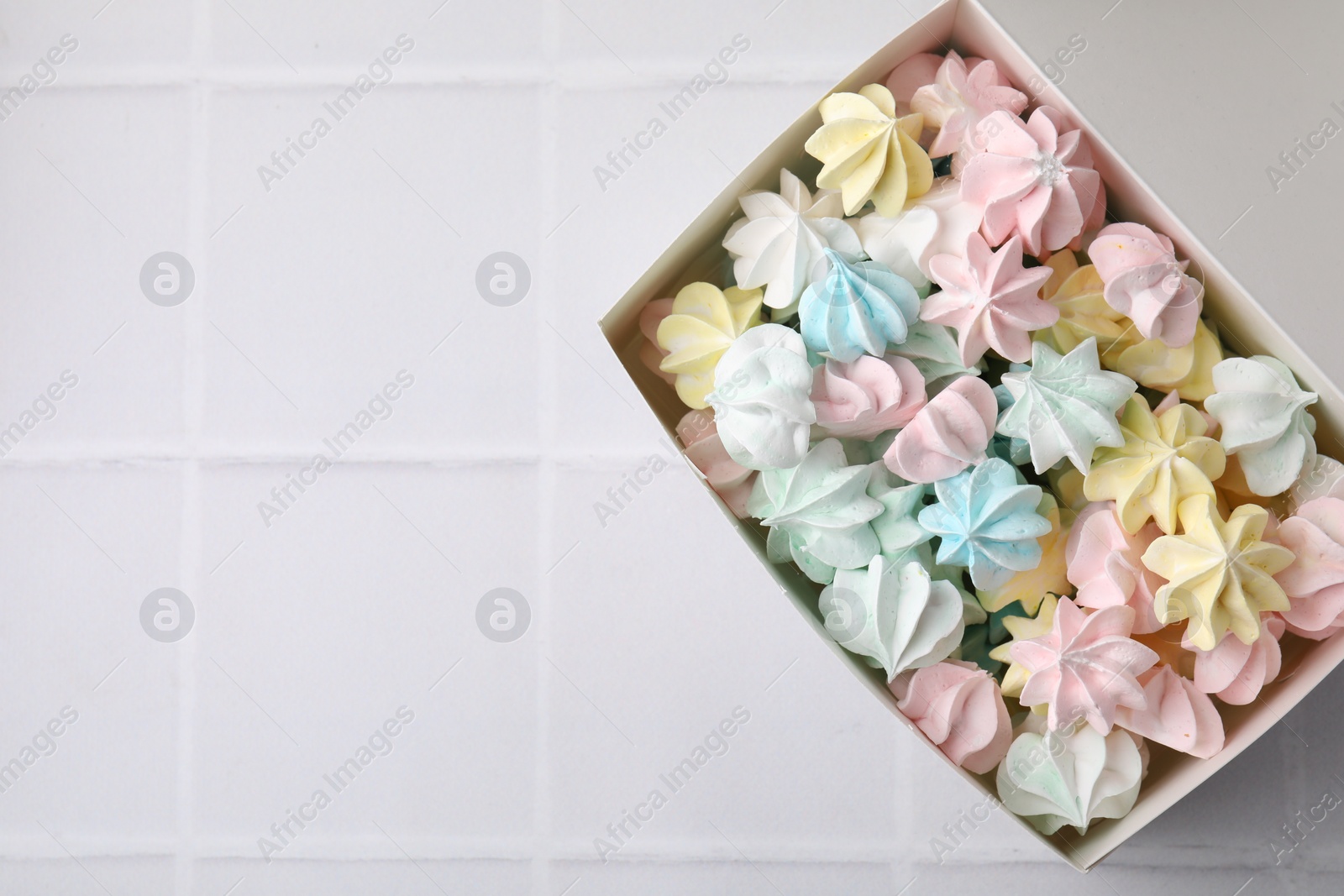 Photo of Tasty meringue cookies on white tiled table, top view. Space for text