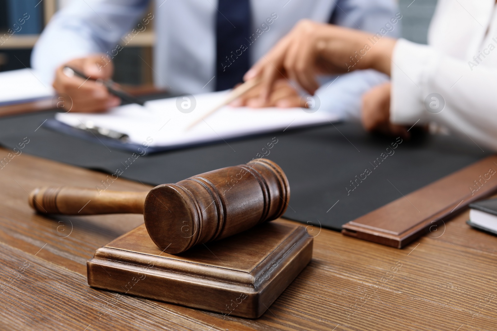 Photo of Wooden gavel and blurred lawyer with client on background