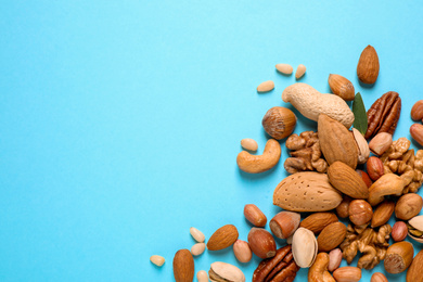 Different delicious nuts on light blue background, flat lay. Space for text