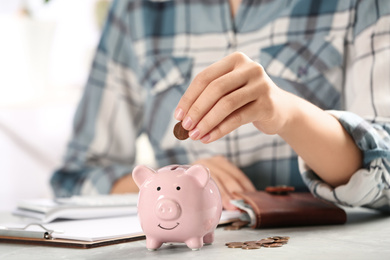 Photo of Woman putting money into piggy bank at table, closeup