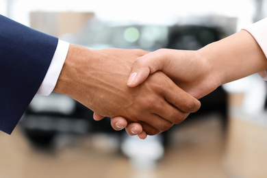 Image of Woman buying car and shaking hands with salesman against blurred auto, closeup