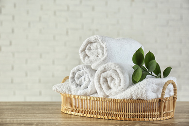 Photo of Wicker basket with rolled bath towels and green branch on wooden table